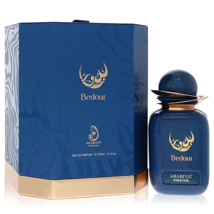 A clear glass bottle with a gold cap and dark amber liquid, standing on a white surface, labeled Arabiyat Prestige Bedour Eau