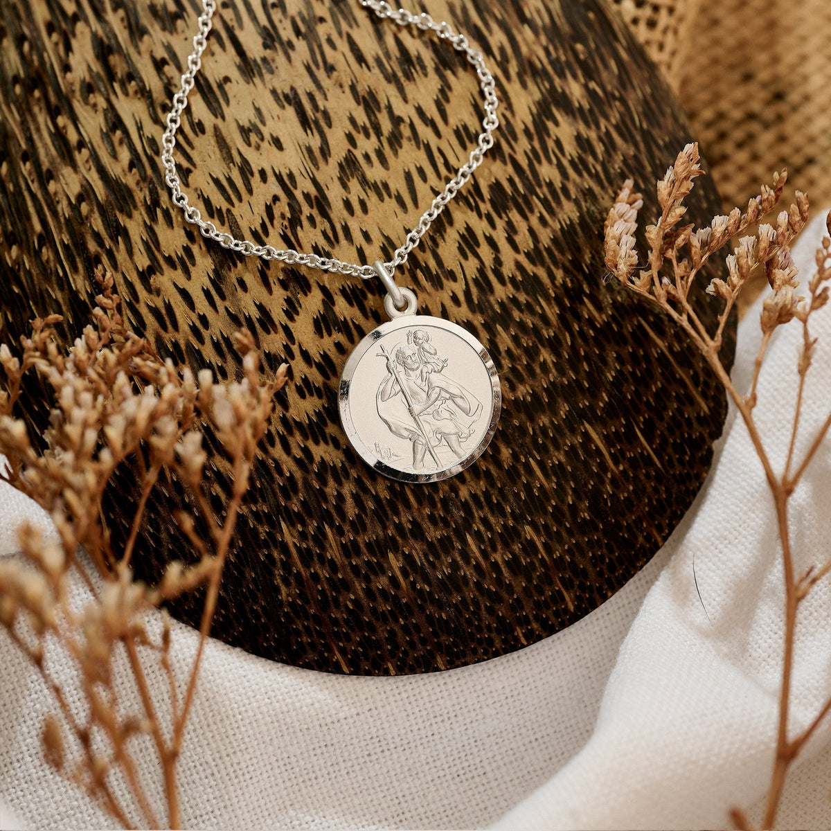 A sterling silver St Christopher pendant hangs on a delicate chain against a white background by Scarlett Jewellery.