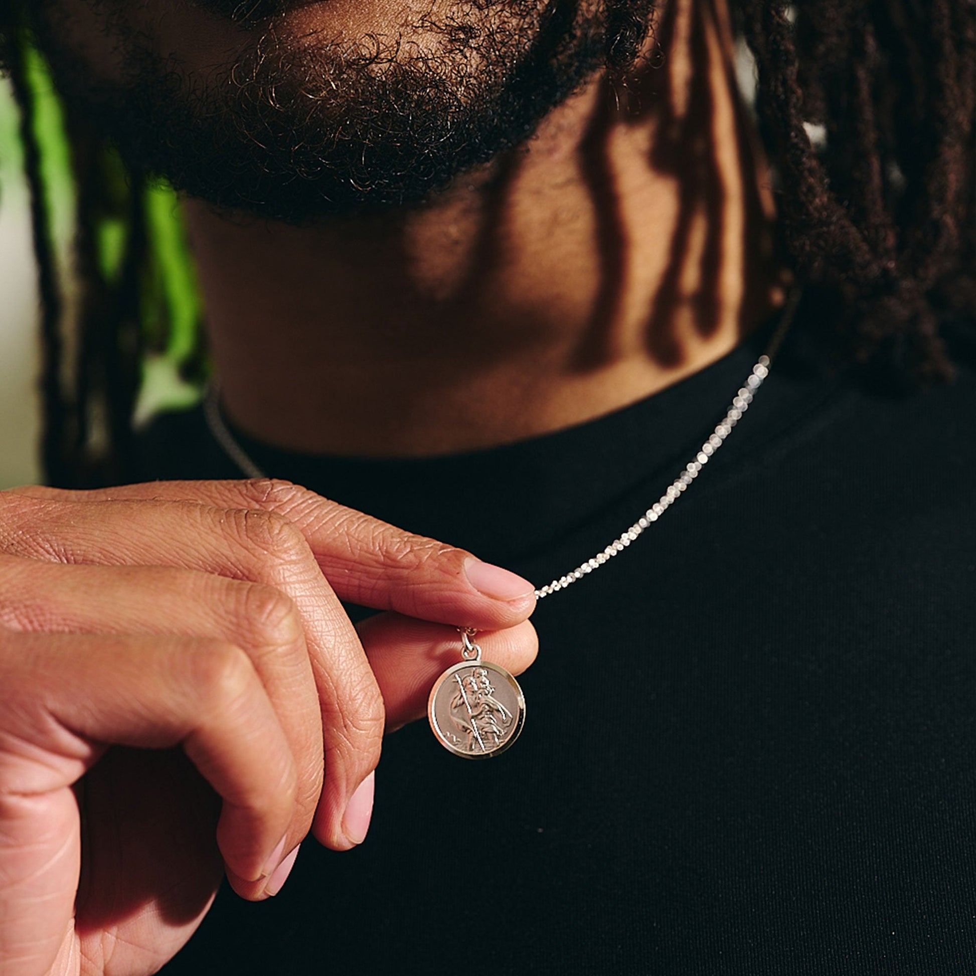 A sterling silver St Christopher pendant hangs on a delicate chain, featuring a detailed 18mm design by Scarlett Jewellery.