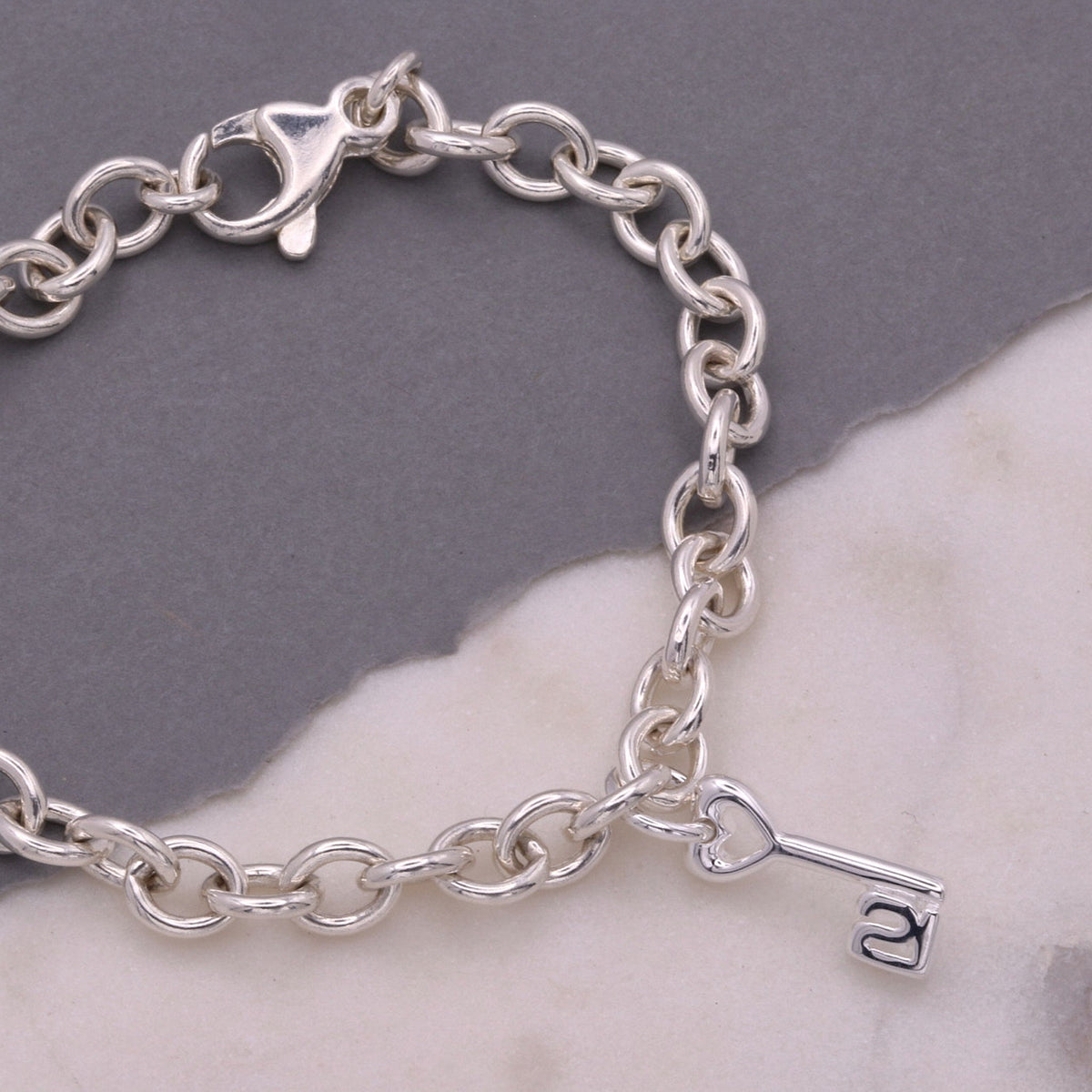 A silver 21st birthday charm displayed on a velvet background by Scarlett Jewellery.