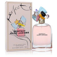 A clear glass perfume bottle with gold accents and a white label featuring the brand name, displayed on a wooden surface.