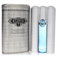 Blue glass bottle with gold accents, standing on a wooden surface, labeled "Cuba Prestige Platinum" by Fragluxe Eau de Toilet