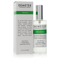A clear glass bottle of Demeter Mistletoe Cologne Spray with a white label and gold accents, standing on a wooden surface by 