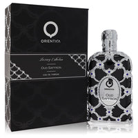 A dark glass bottle of Al Haramain Orientica Oud Saffron Eau De Parfum Spray 5 oz with gold accents on a wooden table by The 