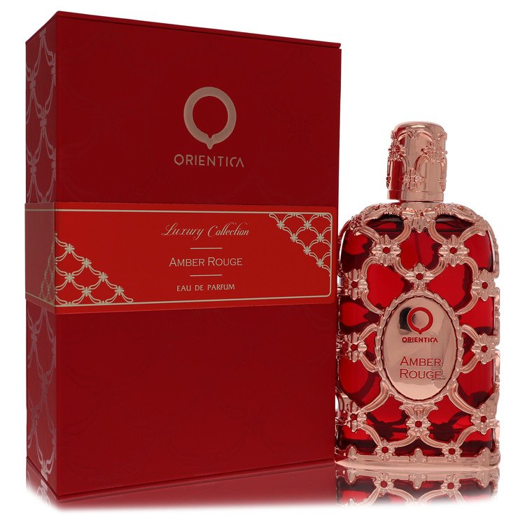 A clear glass bottle with amber liquid and a red label, standing on a wooden surface, labeled "Orientica Amber Rouge Unisex E