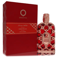 A clear glass bottle with amber liquid and a red label, standing on a wooden surface, labeled "Orientica Amber Rouge Unisex E