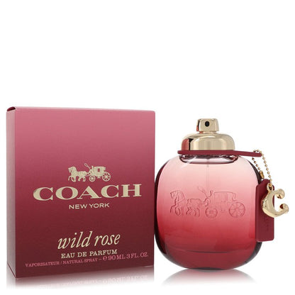 A clear glass perfume bottle with a pink rose design and gold accents, labeled "Coach Wild Rose Eau de Parfum" on a white bac