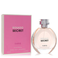 A clear glass perfume bottle with a pink cap and gold label, standing on a white surface, labeled Fariis Rosado Secret Eau De