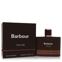 A blue glass bottle with a black cap and white label, featuring the Barbour Origins logo, displayed on a wooden surface by Th
