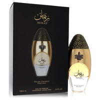 A clear glass bottle with gold accents and a minimalist label, featuring the text Lattafa Niche Emarati Remas, standing on a 
