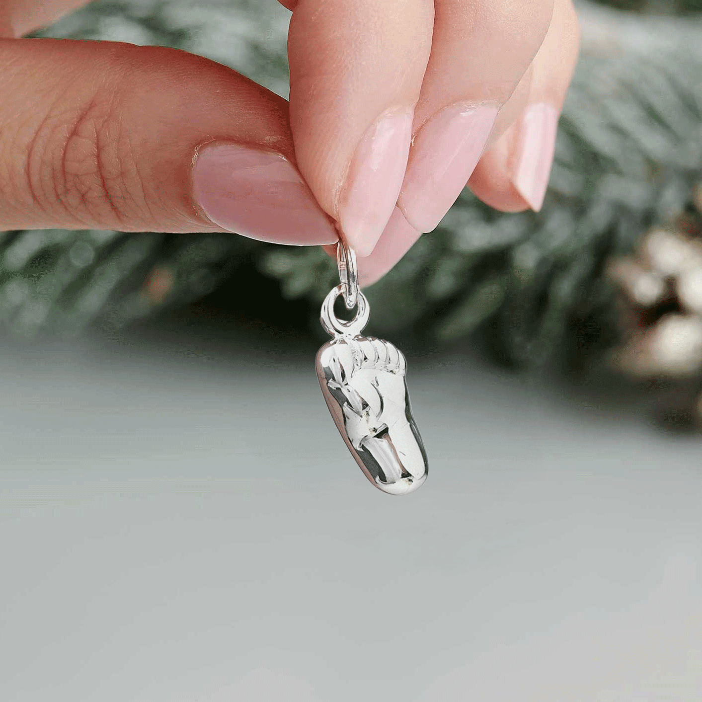 Silver baby charm with personalized engraving, displayed on a soft pink background, by Scarlett Jewellery.
