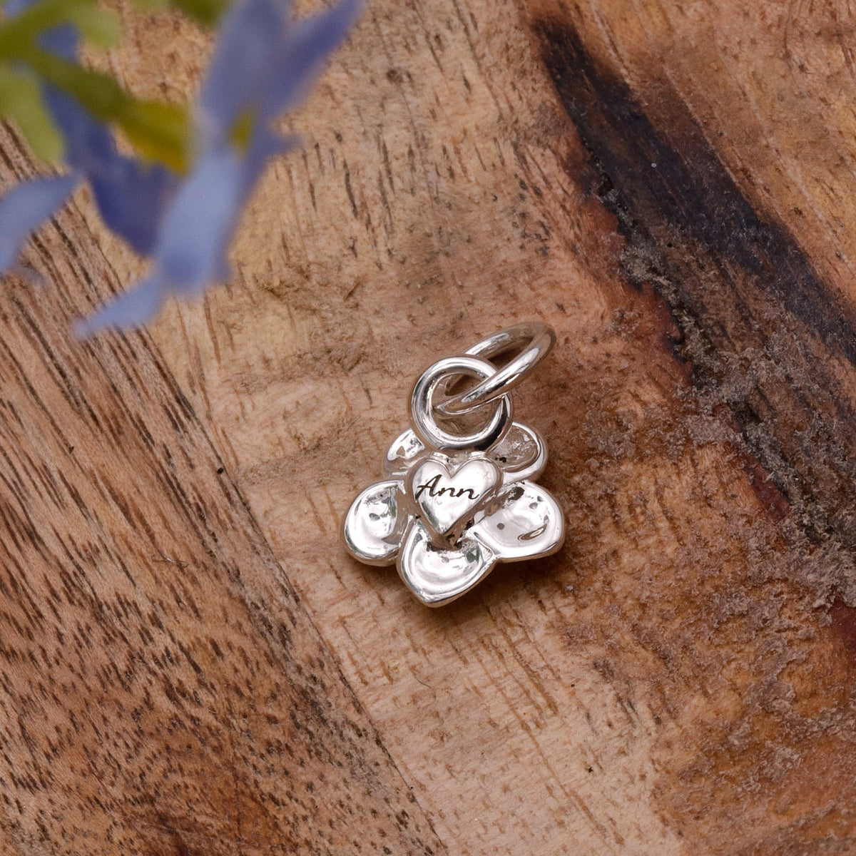 A silver forget-me-not flower charm with personalized engraving, displayed on a soft white background by Scarlett Jewellery.