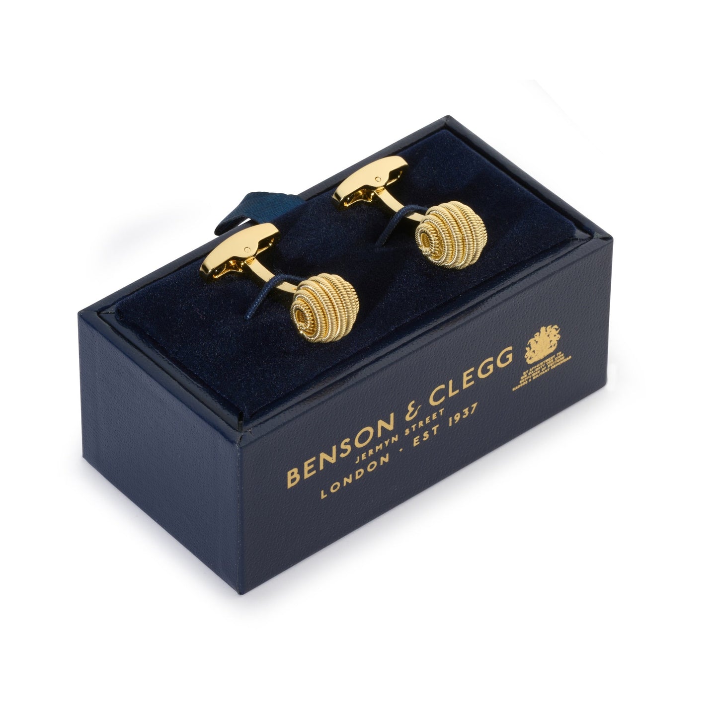Gold spiral cufflinks with intricate detailing, styled on a dark fabric background, by Benson & Clegg.