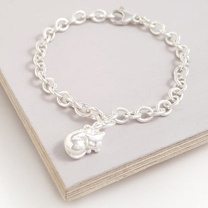 A silver cat charm with intricate detailing, displayed on a soft pink background, by Scarlett Jewellery.