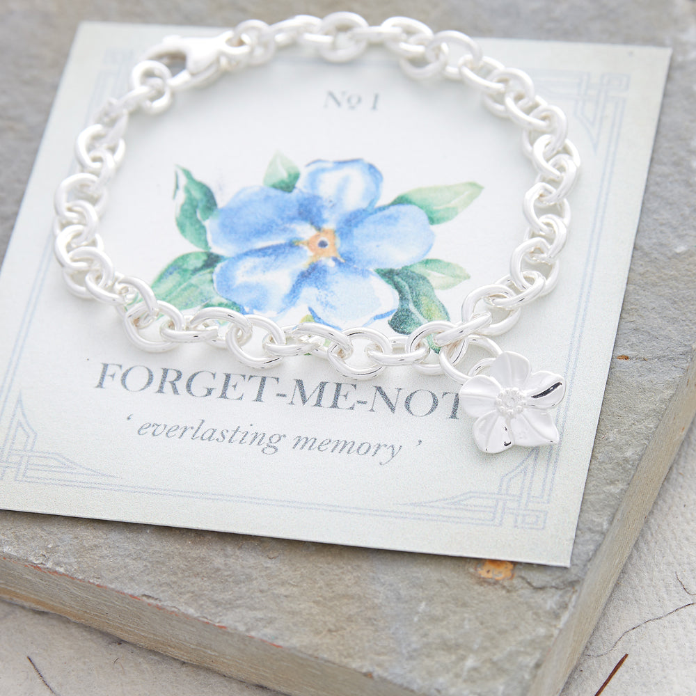 A silver personalised charm bracelet with a forget-me-not design worn on the wrist by Scarlett Jewellery.