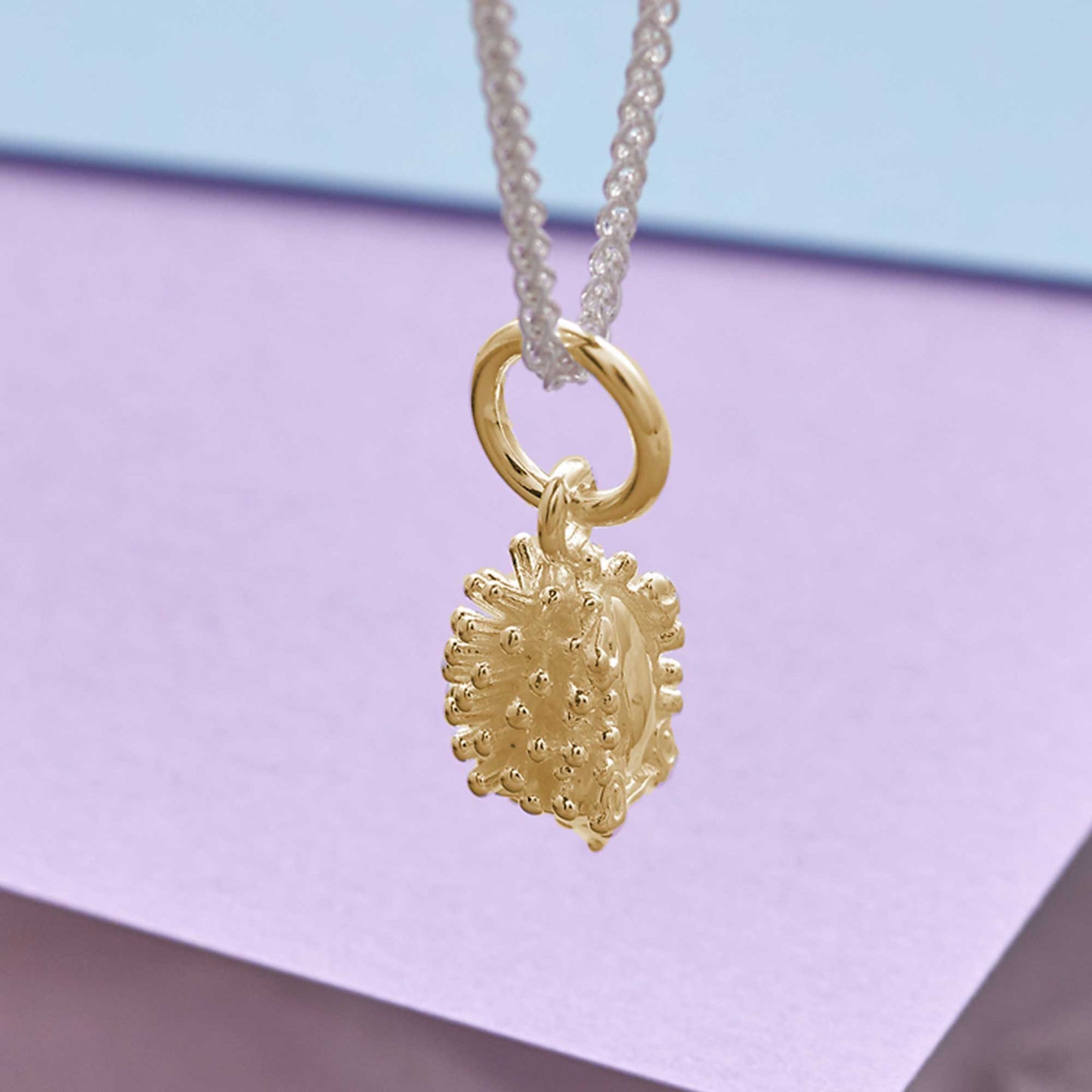 A silver hedgehog charm shaped like a small ball, detailed with texture and spikes, by Scarlett Jewellery.