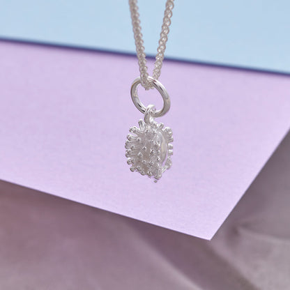 Silver hedgehog charm with intricate detailing, displayed on a soft fabric background, by Scarlett Jewellery.