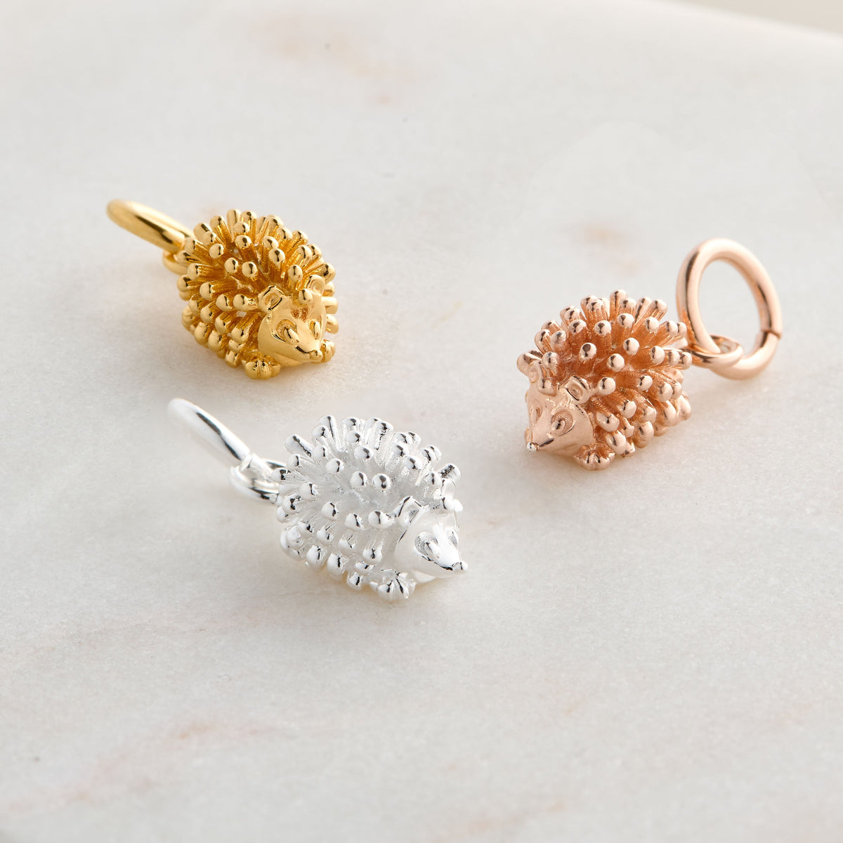 A silver hedgehog charm shaped like a small ball, detailed with texture and spikes, by Scarlett Jewellery.