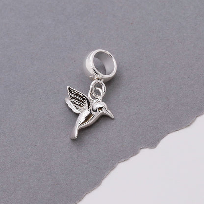 A silver hummingbird charm shaped like a delicate winged bird, featured on a soft white background by Scarlett Jewellery.