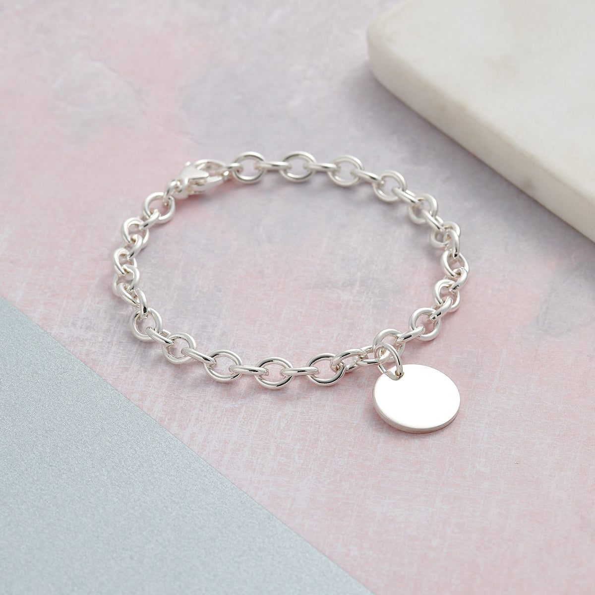 A silver round tag charm bracelet with personalized engraving, featuring a delicate chain and circular design by Scarlett Jew