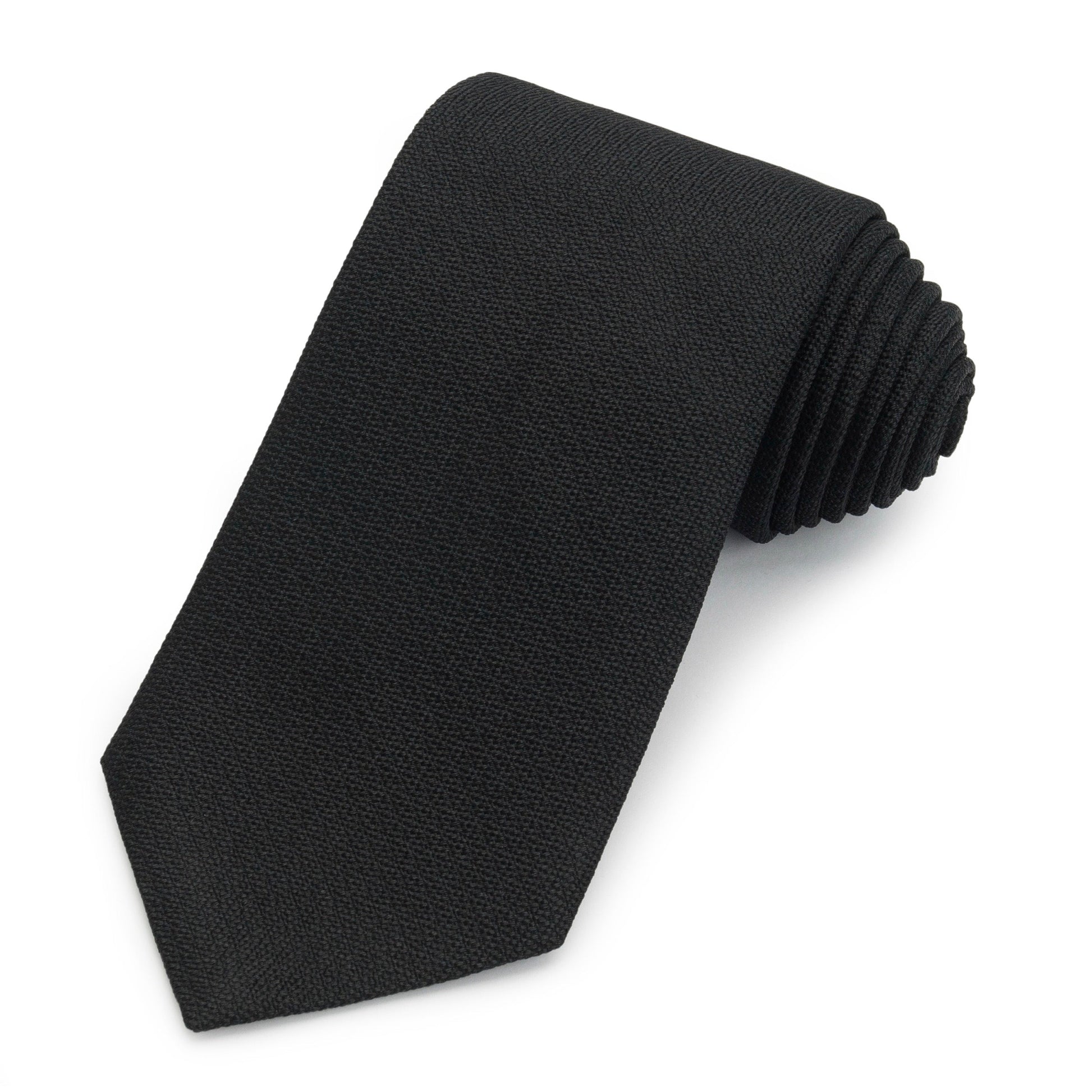 Black three-fold silk tie in non-crease weave displayed on a wooden table by Benson & Clegg.