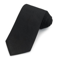 Black three-fold silk tie in non-crease weave displayed on a wooden table by Benson & Clegg.