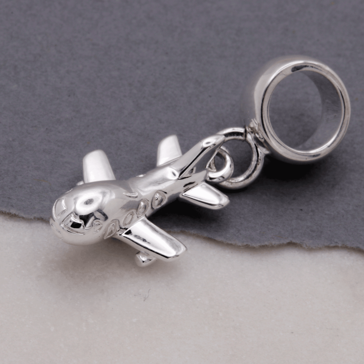 Aeroplane silver charm with detailed wing texture, displayed on a soft fabric background by Scarlett Jewellery.