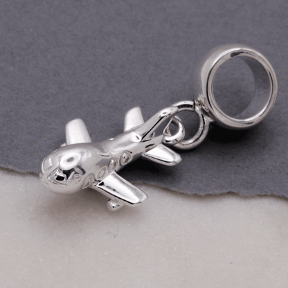 Aeroplane silver charm with detailed wing texture, displayed on a soft fabric background by Scarlett Jewellery.