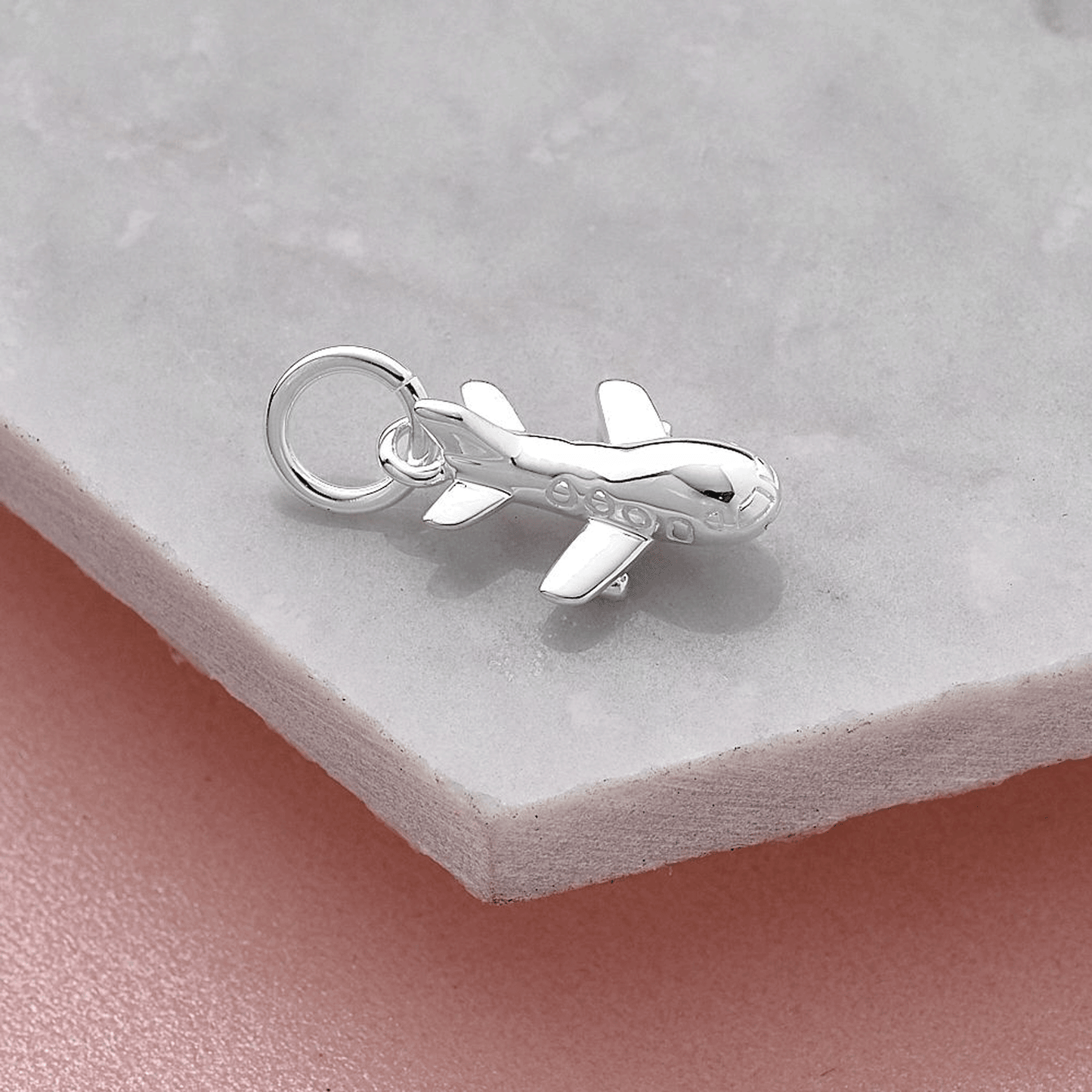 Aeroplane silver charm with intricate detailing, displayed on a soft pink background by Scarlett Jewellery.