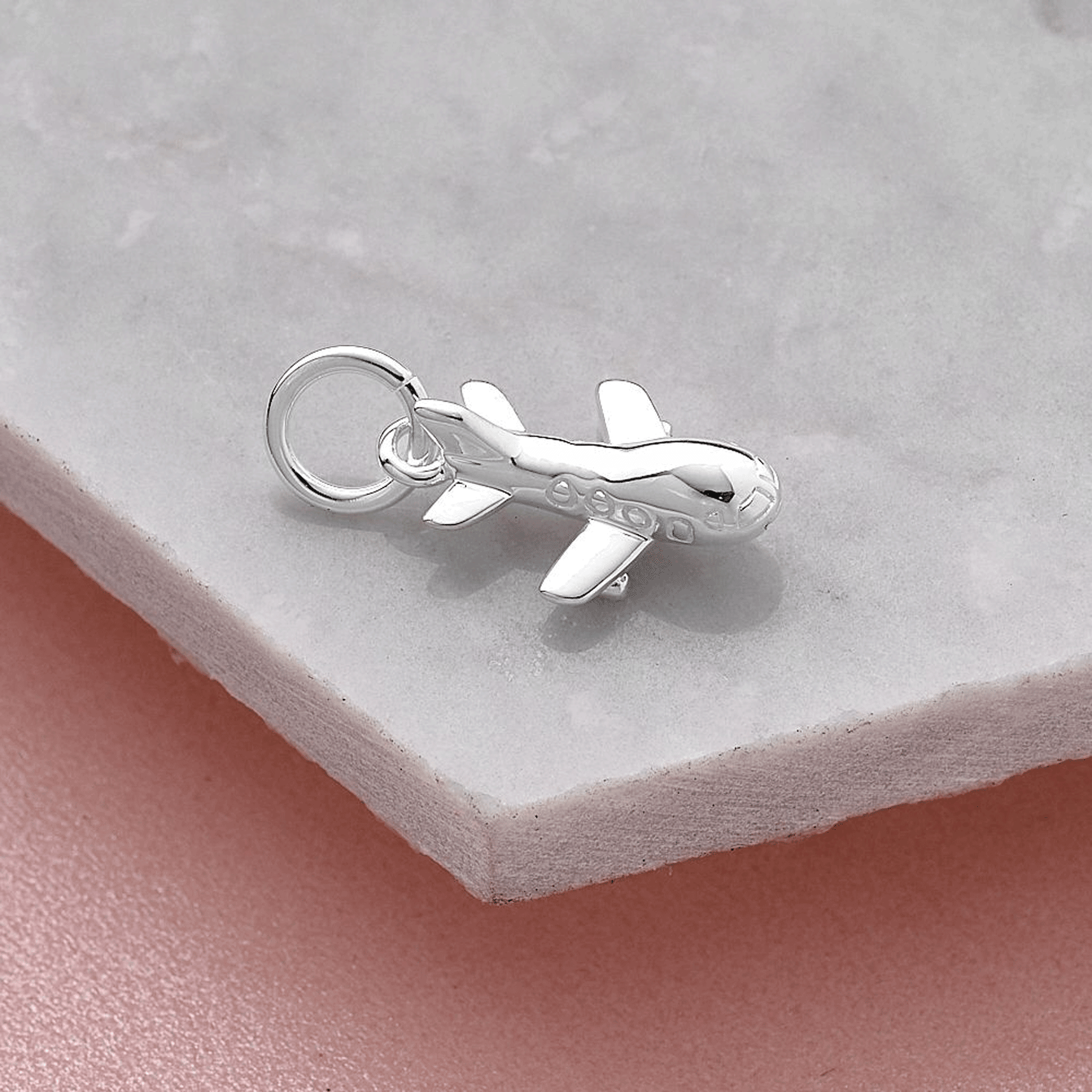 Aeroplane silver charm with intricate detailing, displayed on a soft pink background by Scarlett Jewellery.