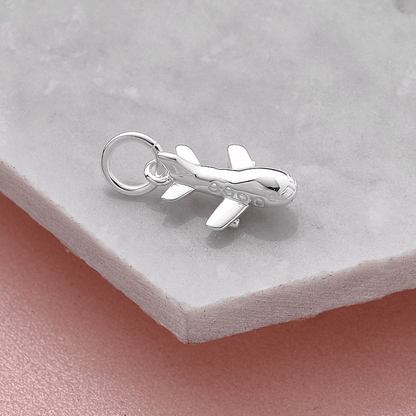 Aeroplane silver charm with intricate detailing, displayed on a soft pink background by Scarlett Jewellery.