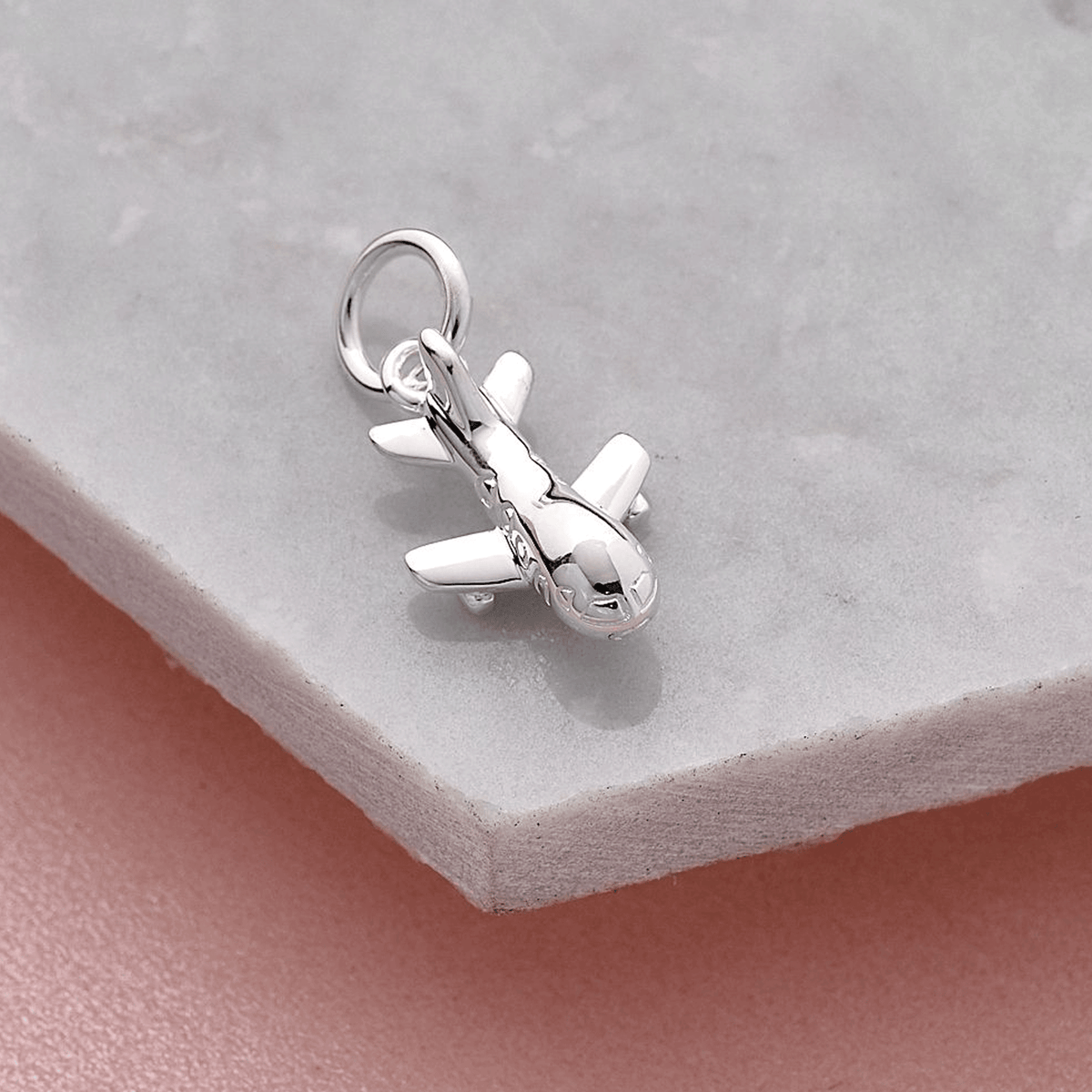 Aeroplane silver charm with intricate detailing, displayed on a soft pink background by Scarlett Jewellery.