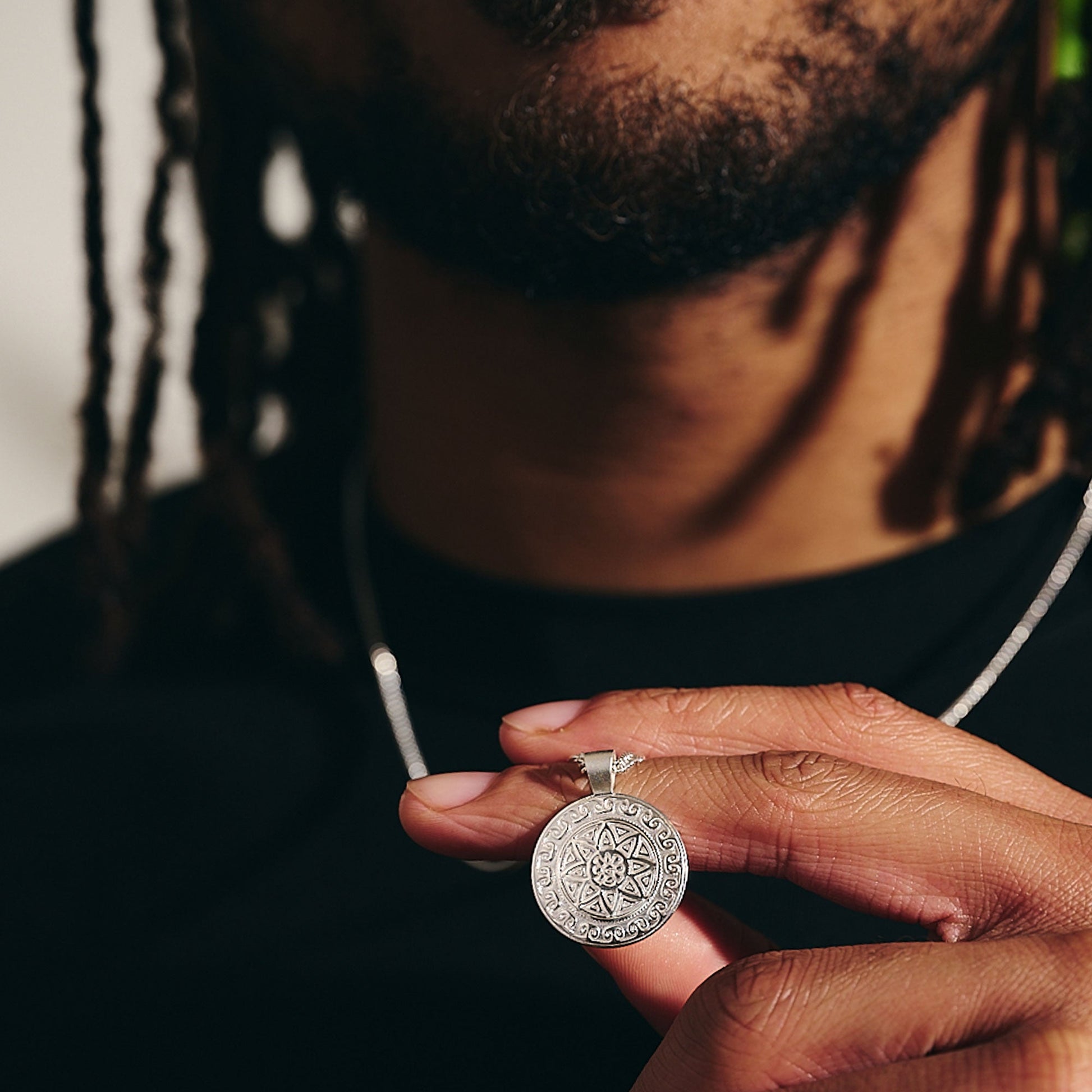 A silver mandala necklace with intricate Aztec Ollin design worn on a chain by Scarlett Jewellery.