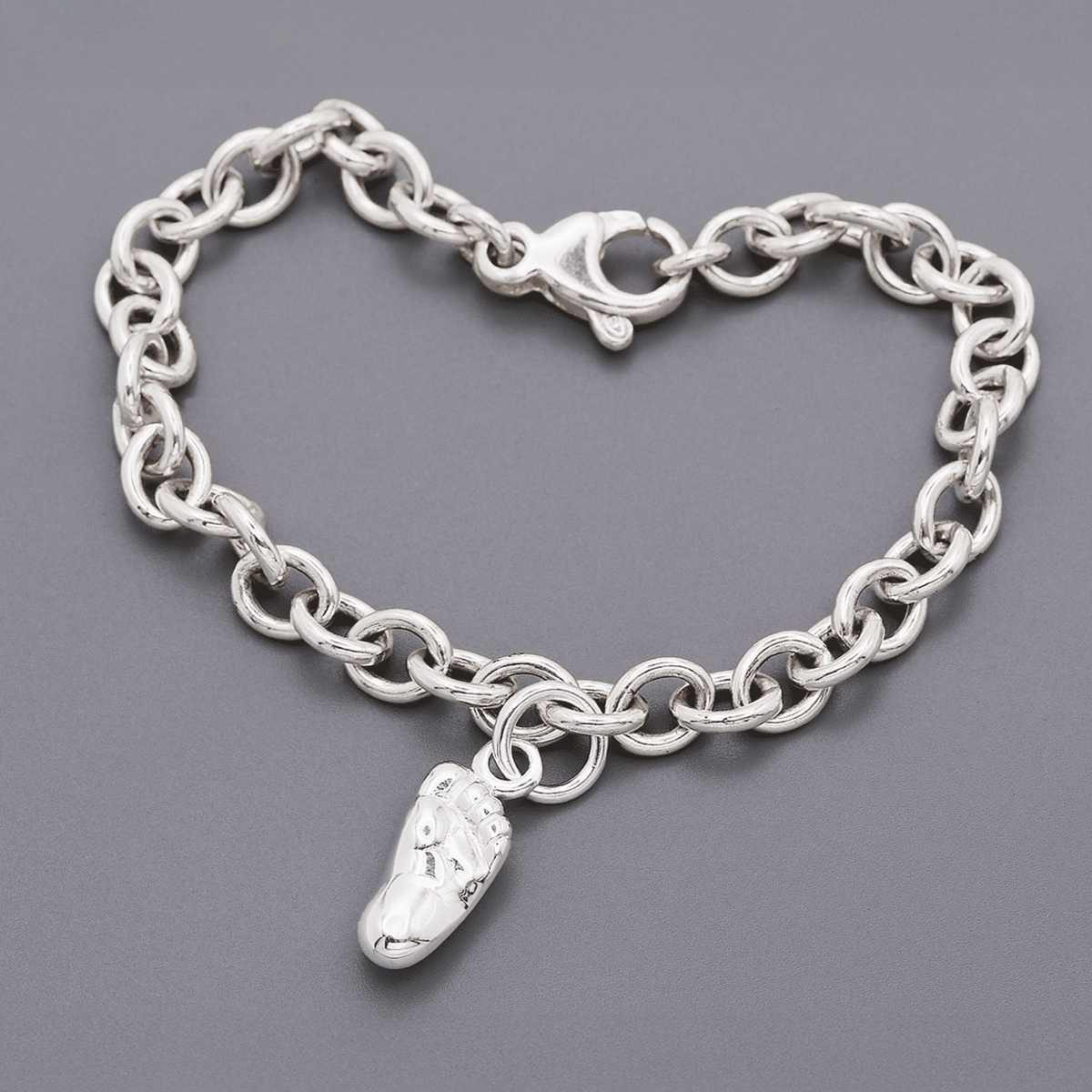 Silver baby charm with personalized engraving, displayed on a soft pink background, by Scarlett Jewellery.