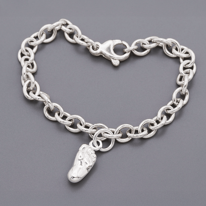 Silver baby charm with personalized engraving, displayed on a soft pink background, by Scarlett Jewellery.