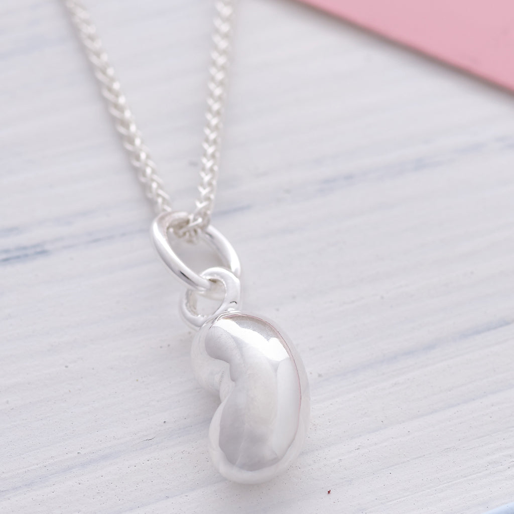Silver baby bean charm with delicate detailing, displayed on a white background by Scarlett Jewellery.