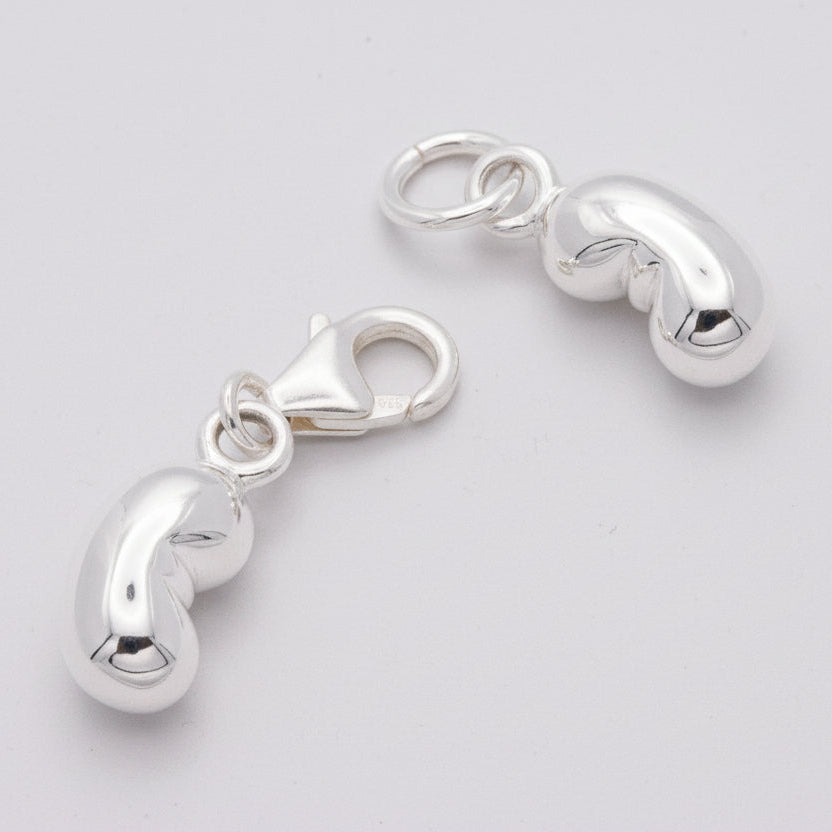 A silver baby bean charm hangs from a chain, detailed and reflective, by Scarlett Jewellery.