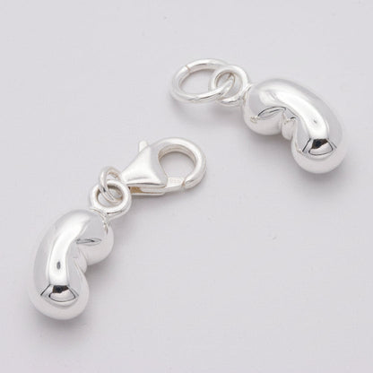 A silver baby bean charm hangs from a chain, detailed and reflective, by Scarlett Jewellery.