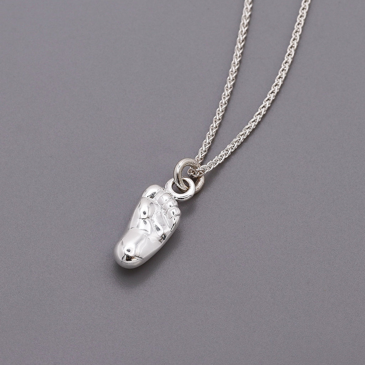 A silver baby charm with personalized engraving, displayed on a soft pink background, by Scarlett Jewellery.