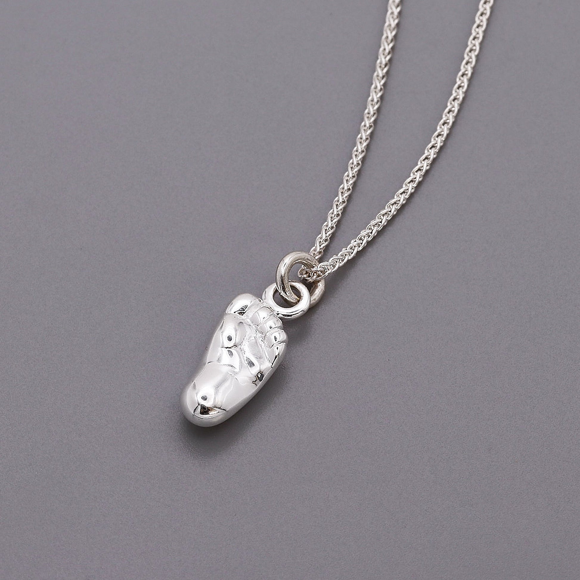 A silver baby charm with personalized engraving, displayed on a soft pink background, by Scarlett Jewellery.