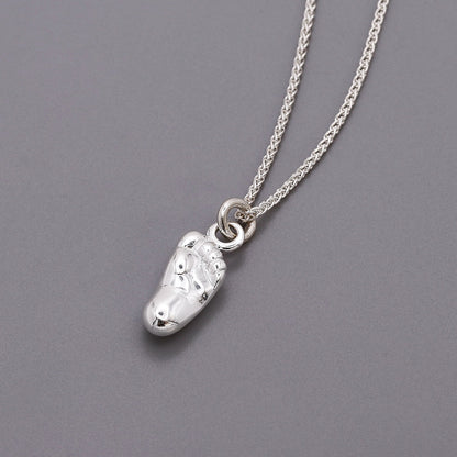 A silver baby charm with personalized engraving, displayed on a soft pink background, by Scarlett Jewellery.