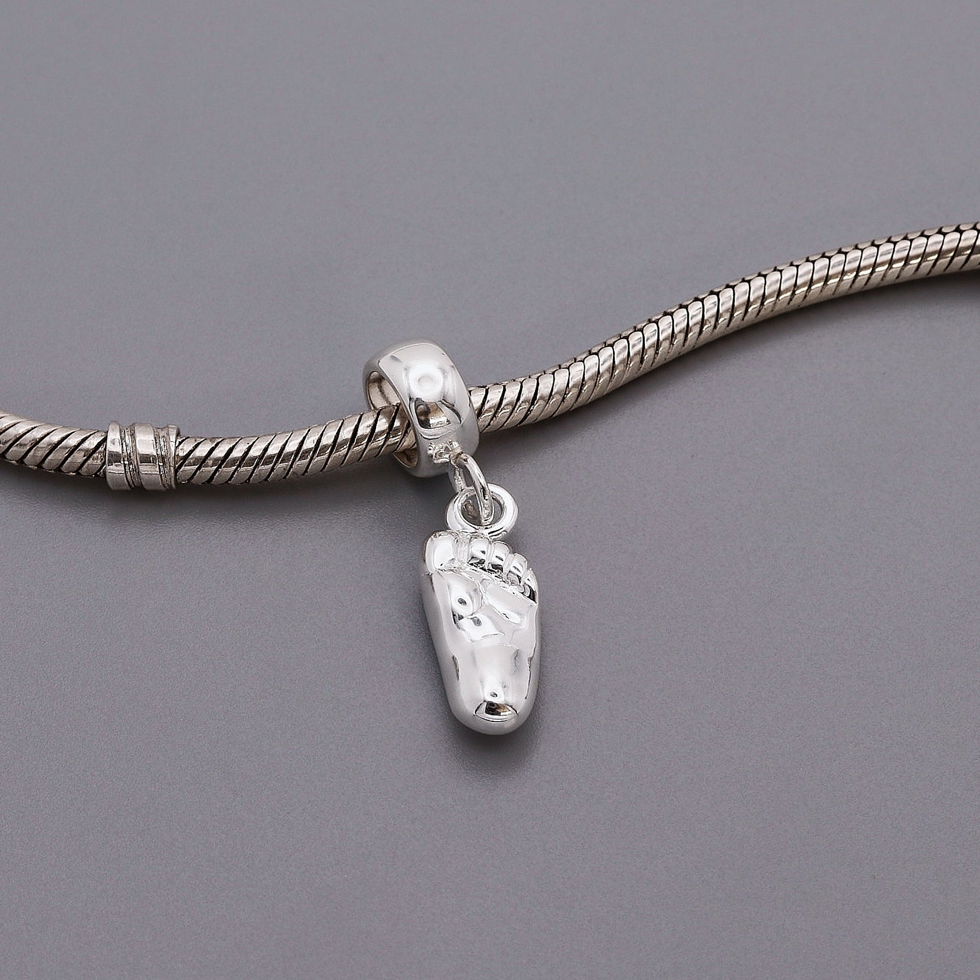 A silver baby charm with personalized engraving, displayed on a soft pink background, by Scarlett Jewellery.
