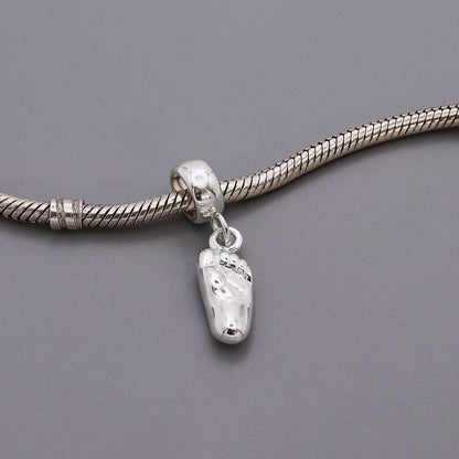 A silver baby charm with personalized engraving, displayed on a soft pink background, by Scarlett Jewellery.