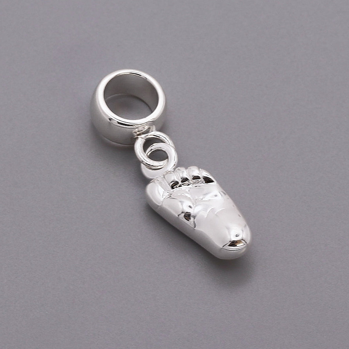 Silver baby charm with personalized engraving, displayed on a soft pink background, by Scarlett Jewellery.