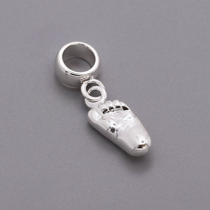 Silver baby charm with personalized engraving, displayed on a soft pink background, by Scarlett Jewellery.