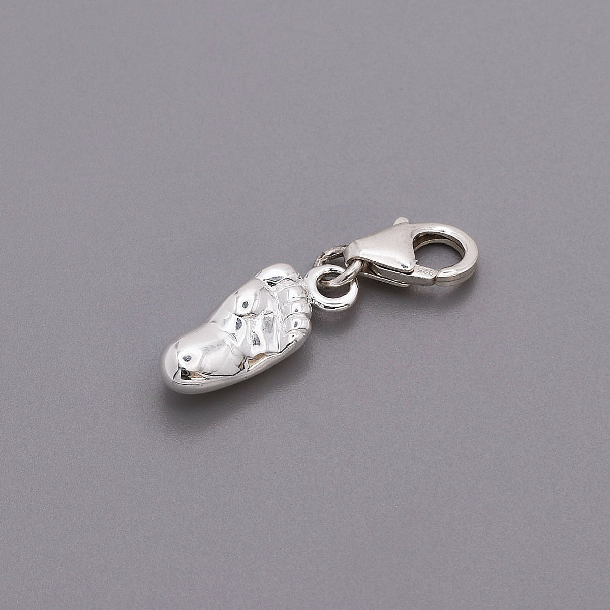 A silver baby charm with personalized engraving, displayed on a soft pink background, by Scarlett Jewellery.