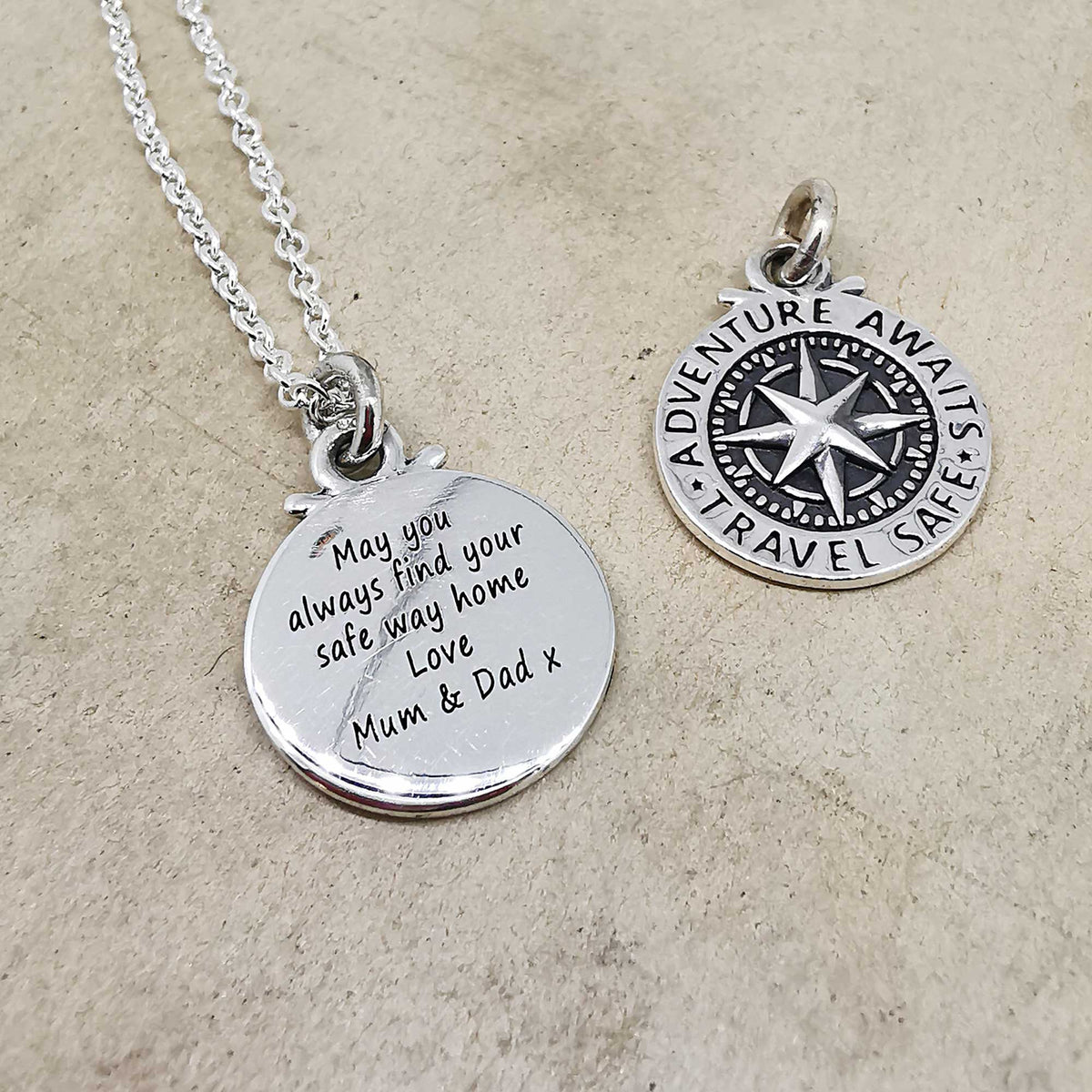 Silver compass charm with personalized engraving, styled on a travel-themed background by Scarlett Jewellery.