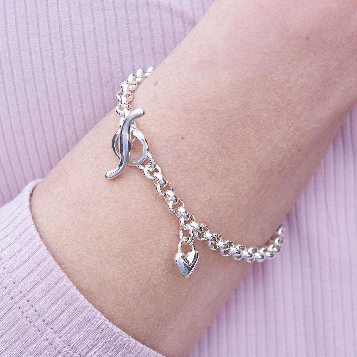 A silver heart chain charm bracelet with a detailed heart pendant, showcasing intricate design and craftsmanship by Scarlett 