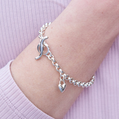 A silver heart chain charm bracelet with a detailed heart pendant, showcasing intricate design and craftsmanship by Scarlett 