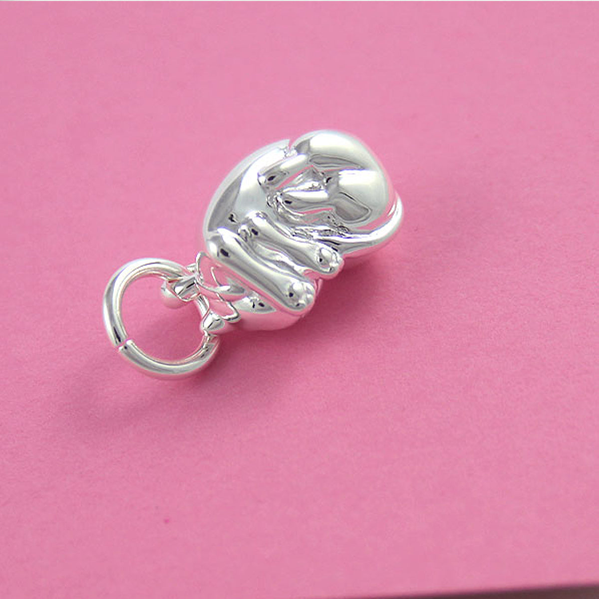 A silver cat charm with intricate detailing, displayed on a soft fabric background, by Scarlett Jewellery.